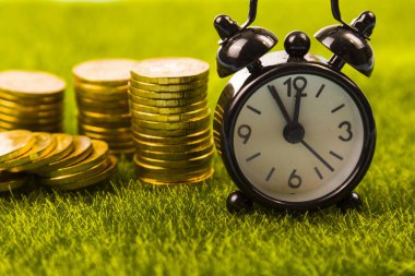 Çalar saat ve sikkeler çimenlerin üzerinde.