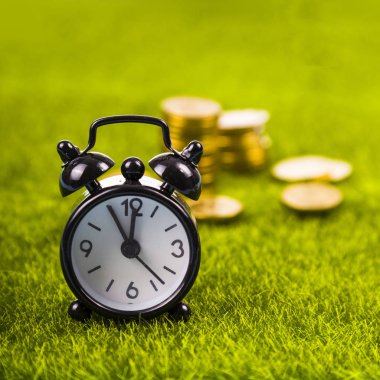 Çalar saat ve sikkeler çimenlerin üzerinde.