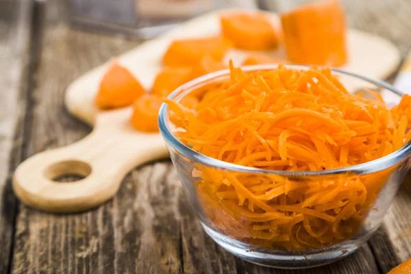 Ahşap bir masa üzerinde bir kapta havuç rendeleyin. 