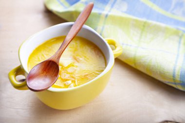 Ahşap bir masa üzerinde sarı bir tabak içinde peynir çorbası. Lezzetli akşam yemeği.