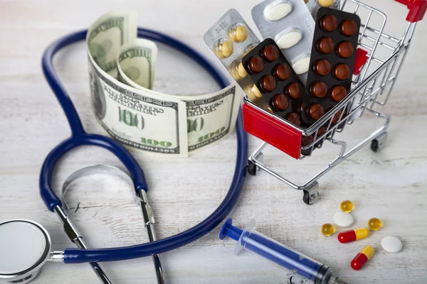 Shopping cart with pills,money and calculator on a wooden background. Paid medicine.