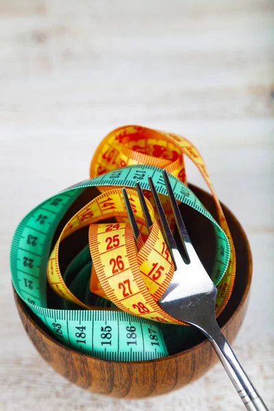 Measuring tape in a wooden bowl and fork. — Stock Photo, Image