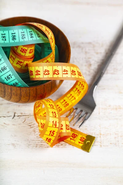 Measuring tape in a wooden bowl and fork. — Stock Photo, Image