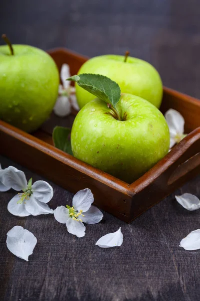 Gröna äpplen, blommor och blad på en träbricka. — Stockfoto