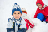 Hravý veselý děti sáňkování a sněhulák v sněhu