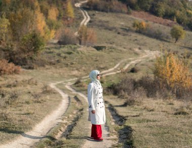 Genç ve çekici bir kadın sonbahar yolunda duruyor.