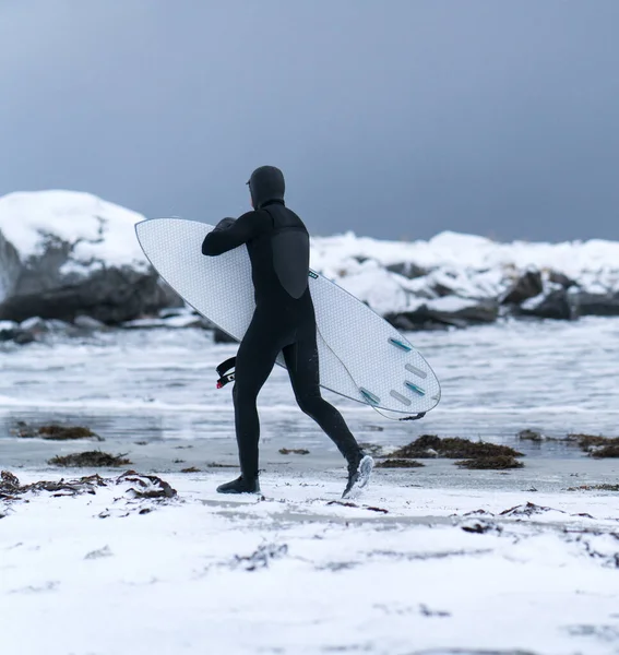 Серфингист, гуляющий по зимнему снежному пляжу — стоковое фото