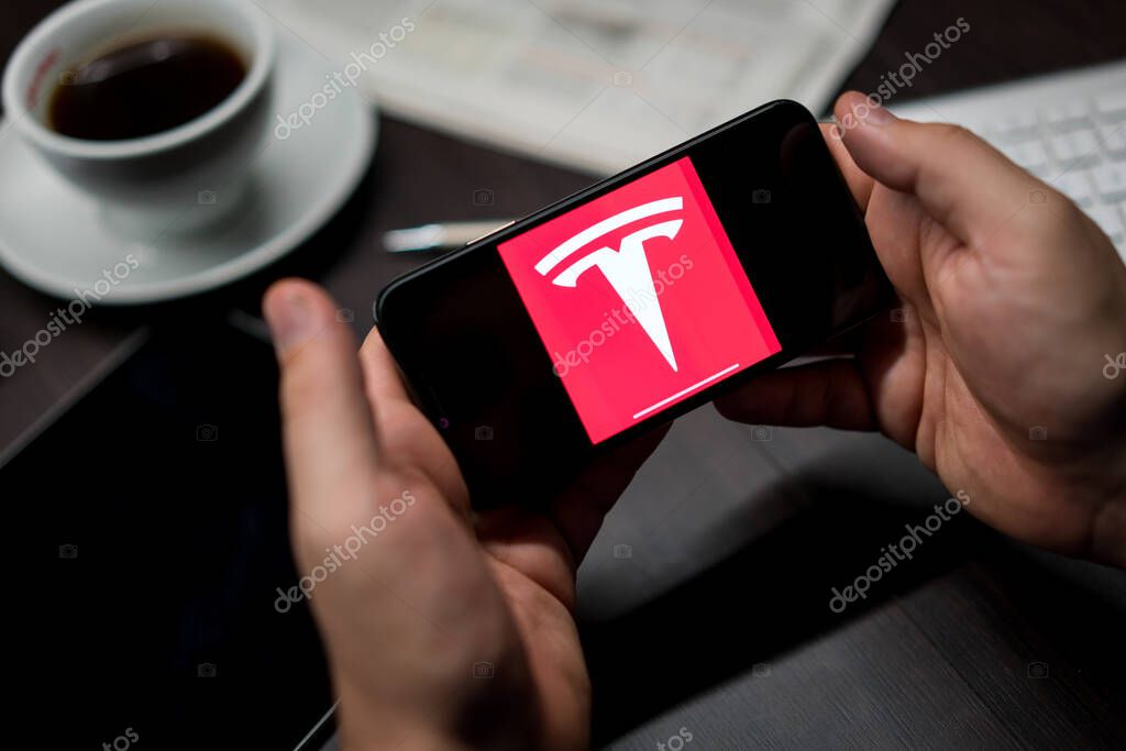 New York, New York / USA - 11 11 2019: Logo of Tesla on the iPhone X in hands in office