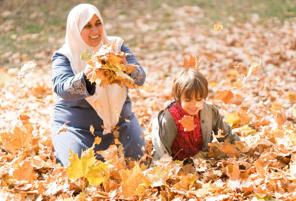 Muslim mother with little son in autumn leaves