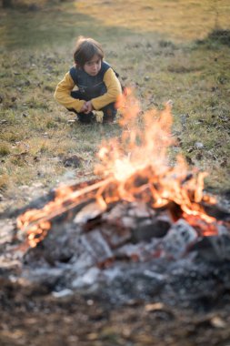 Çayırda kamp ateşinin yanında oturan çocuk