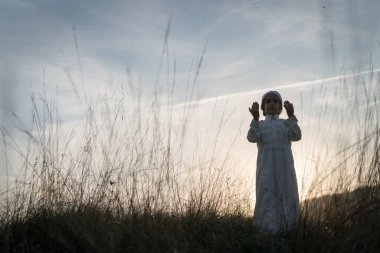 Müslüman çocuk gün batımında çayırda namaz kılıyor