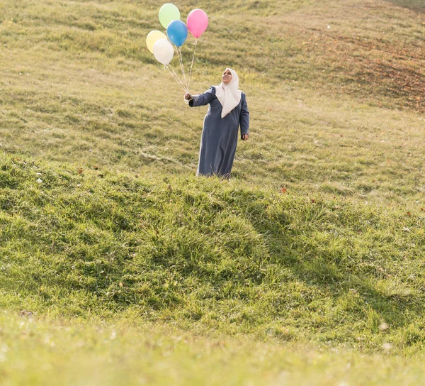 在草绿色草地上拿气球的穆斯林妇女 — 图库照片