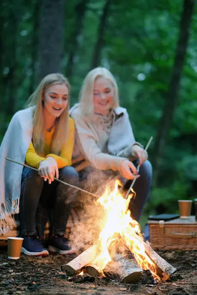 Travel and explore. Two young beautiful women near bonfire in the forest