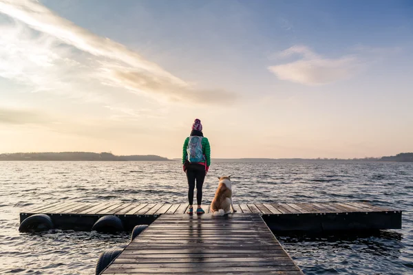 Frau mit Hund genießt Sonnenaufgang am See, Backpacker — Stockfoto
