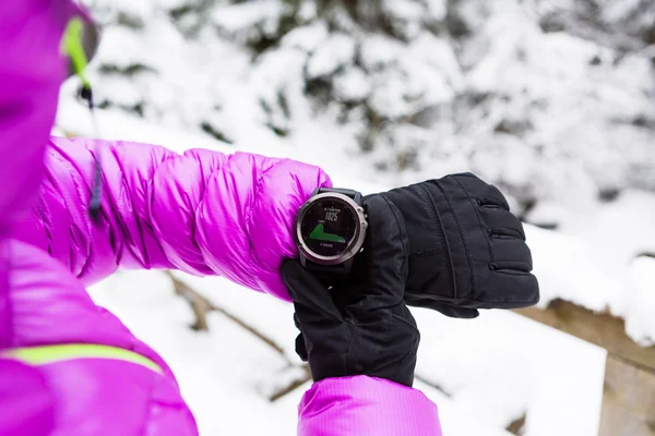 Kobieta wycieczkowicz sprawdzanie zegarka sportowego w zimie lasy i góry — Zdjęcie stockowe