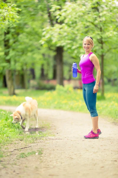 Donna che corre e fa jogging con cane nel verde parco estivo e legno — Foto Stock