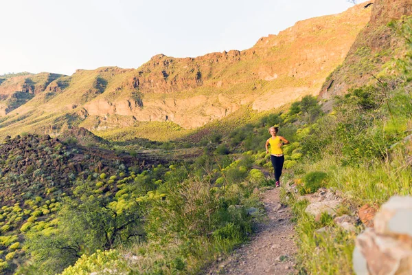 Mujer joven corriendo por sendero de montaña al atardecer —  Fotos de Stock