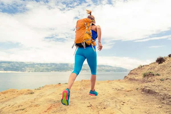 Mujer corriendo con mochila en camino rocoso a orillas del mar —  Fotos de Stock