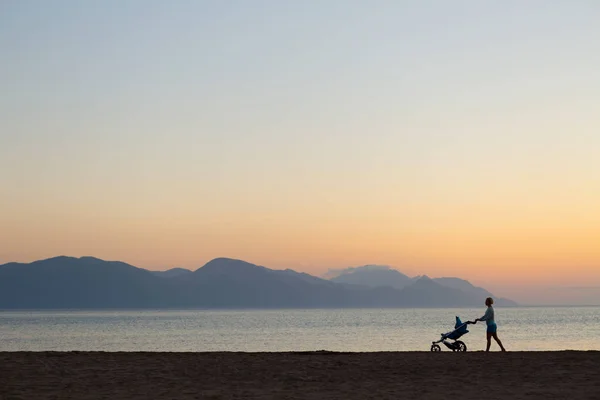 Silhouette of mother with stroller enjoying motherhood at sunset — Stock Photo, Image