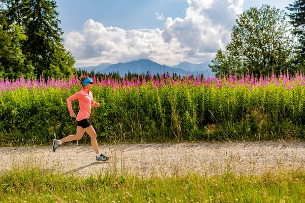 Trilha de mulher correndo na estrada rural nas montanhas, dia de verão — Fotografia de Stock