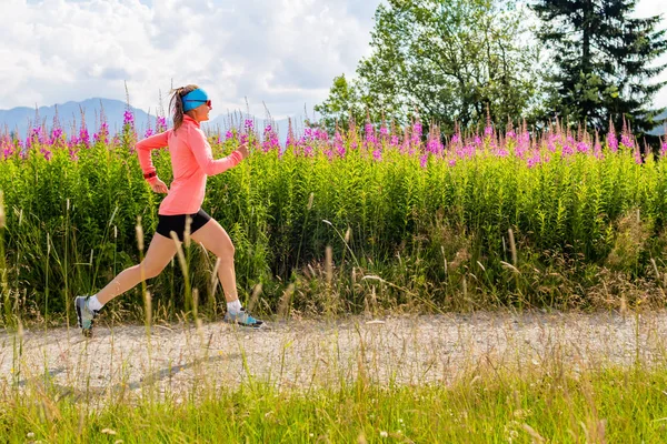 Mujer joven corriendo por el camino del campo en las montañas, día de verano — Foto de Stock