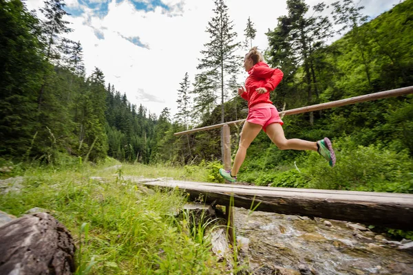 Νεαρή γυναίκα τρέχει στη γέφυρα στα βουνά θερινή ημέρα — Φωτογραφία Αρχείου