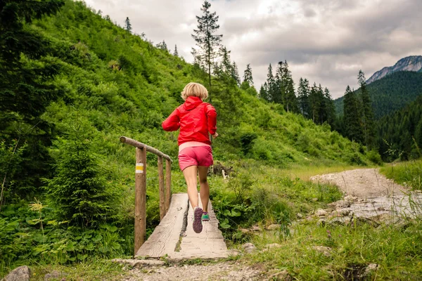 Молодая женщина бежит по мосту в горах в летний день — стоковое фото