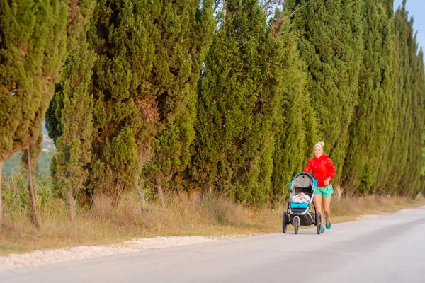 Madre corriendo con cochecito disfrutando de la maternidad en las tierras del atardecer —  Fotos de Stock