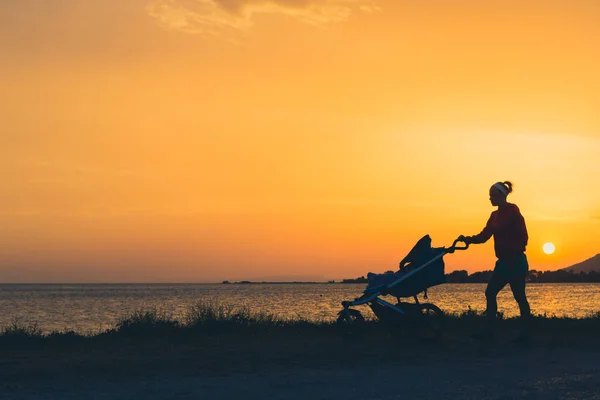 Mãe andando na praia com carrinho desfrutando maternidade — Fotografia de Stock