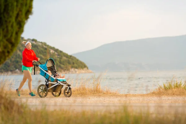 Mãe correndo com carrinho, desfrutando da maternidade no pôr do sol — Fotografia de Stock