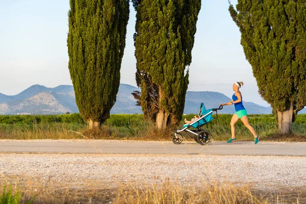 Бегающая мать с коляской наслаждается материнством на закатных землях — стоковое фото