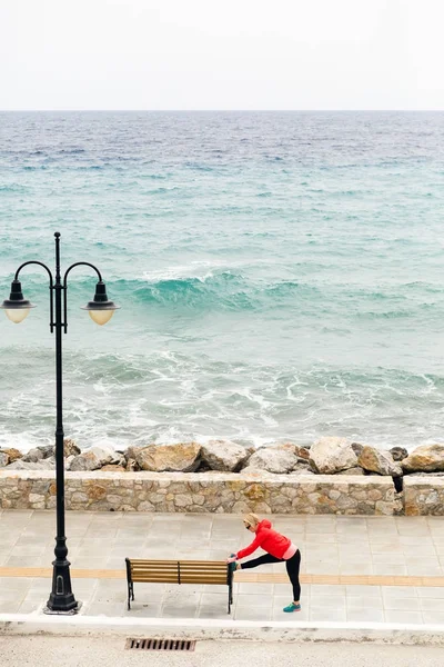 Kvinna utövar och kör på gata, som tittar på havet — Stockfoto