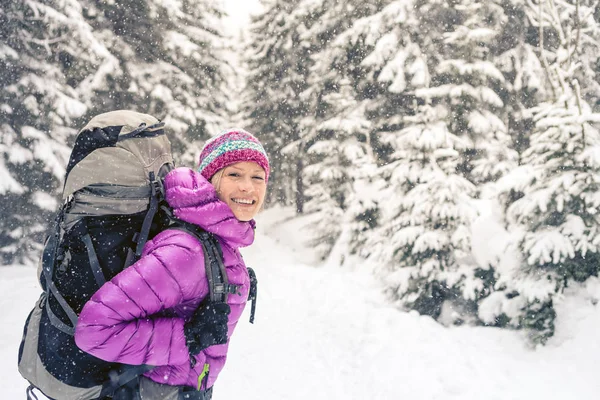 Gelukkige vrouw wandelen in winter woud met rugzak — Stockfoto