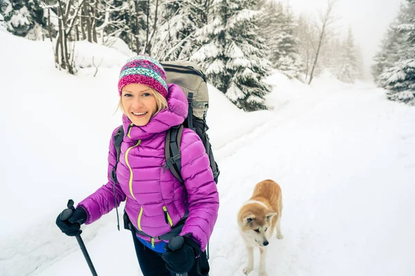Счастливая женщина, гуляющая в зимнем лесу с собакой — стоковое фото