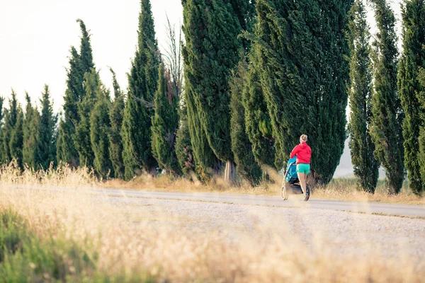 Madre corredora con cochecito de bebé corriendo al atardecer paisaje —  Fotos de Stock