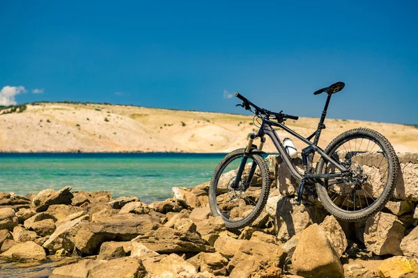 Bicicleta de montaña sobre el mar, montañas y cielo azul en una playa rocosa —  Fotos de Stock