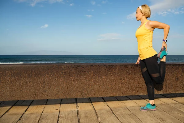 Woman runner stretching at the seaside on sunny summer day — Stock Photo, Image