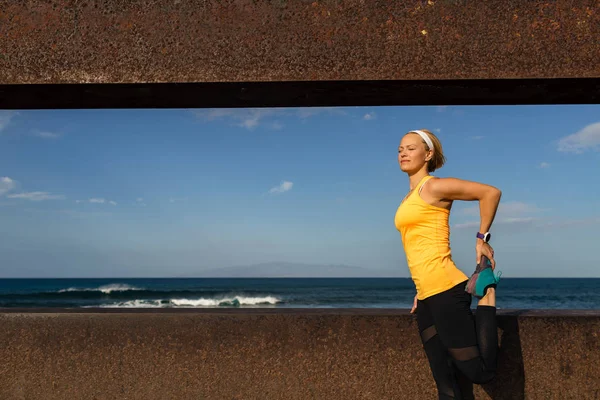 Woman runner stretching at the seaside on sunny summer day — Stock Photo, Image