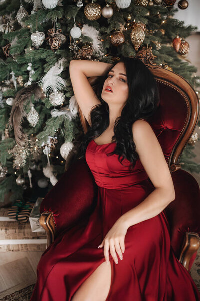 Beautiful woman in red dress posing near Christmas tree  