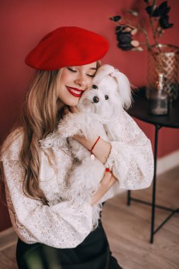 Kırmızı bereli güzel sarışın bir kadının portresi. Beyaz sevimli bir köpekle.