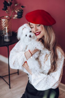 Kırmızı bereli güzel sarışın bir kadının portresi. Beyaz sevimli bir köpekle.