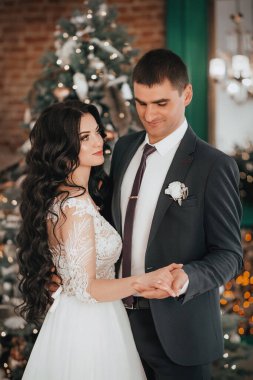 Güzel ve genç gelin ve damat Noel ağacının yanında poz veriyor.