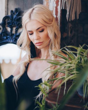 Aynanın yanındaki siyah elbiseli güzel sarışın kadının portresi.