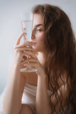 Yatak odasında beyaz çarşaflı genç ve güzel bir kadın.