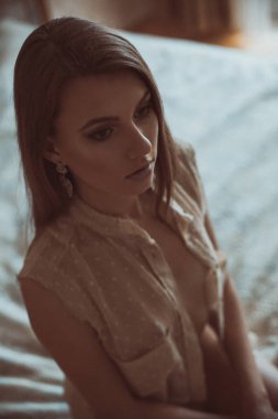 Güzel makyajlı, renkli bir kız yatakta oturuyor ve başka tarafa bakıyor..