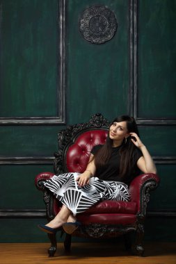 Güzel, pahalı bir sandalyede oturan gülümseyen bir kadının portresi.
