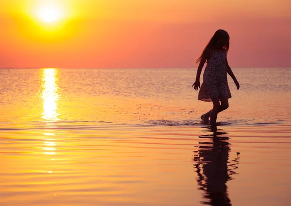 夕焼けの海を歩いて子供の女の子 — ストック写真