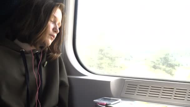 Girl with earphones sleeping at the train near the window — Stock Video
