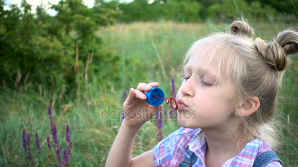 Liten flicka blåser såpbubblor på en grön gräsmatta — Stockvideo