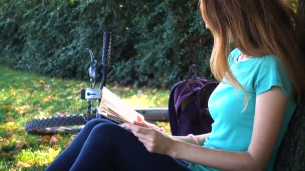 Chica con la bicicleta descansando y leyendo en el parque — Vídeos de Stock